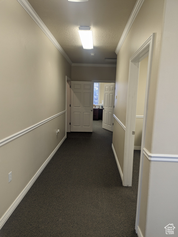 Corridor with ornamental molding, a textured ceiling, and dark carpet