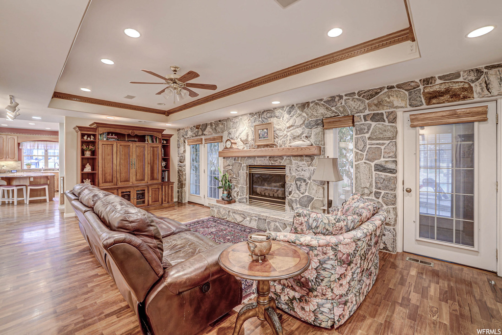 Hardwood floored living room featuring a fireplace, crown molding, ceiling fan, and a tray ceiling