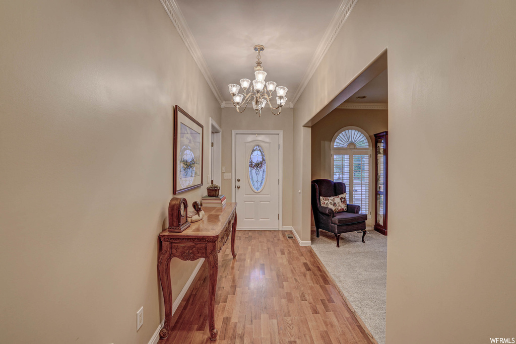 Entryway with light carpet, a notable chandelier, and ornamental molding