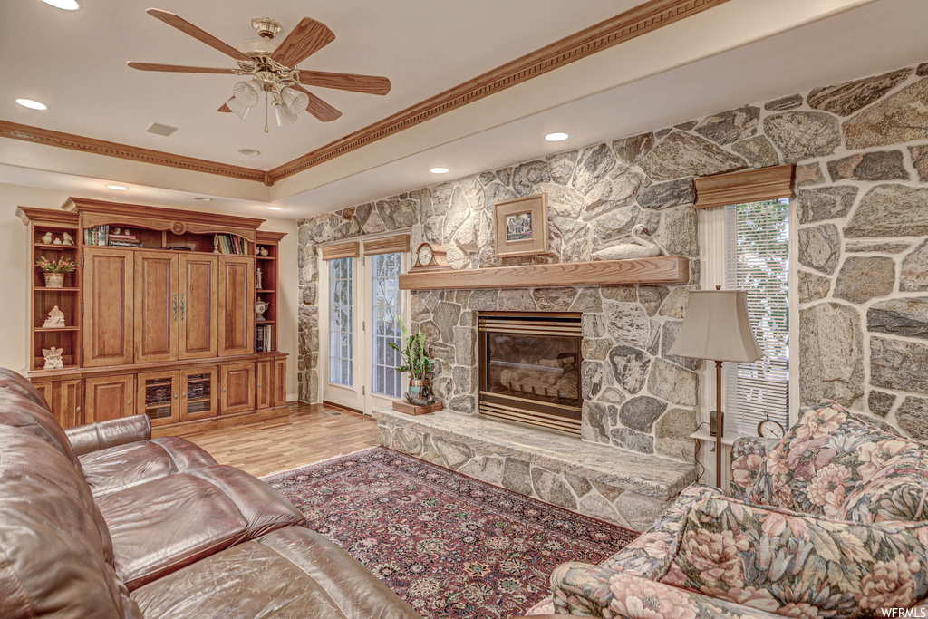 Hardwood floored living room with ornamental molding, a fireplace, and ceiling fan