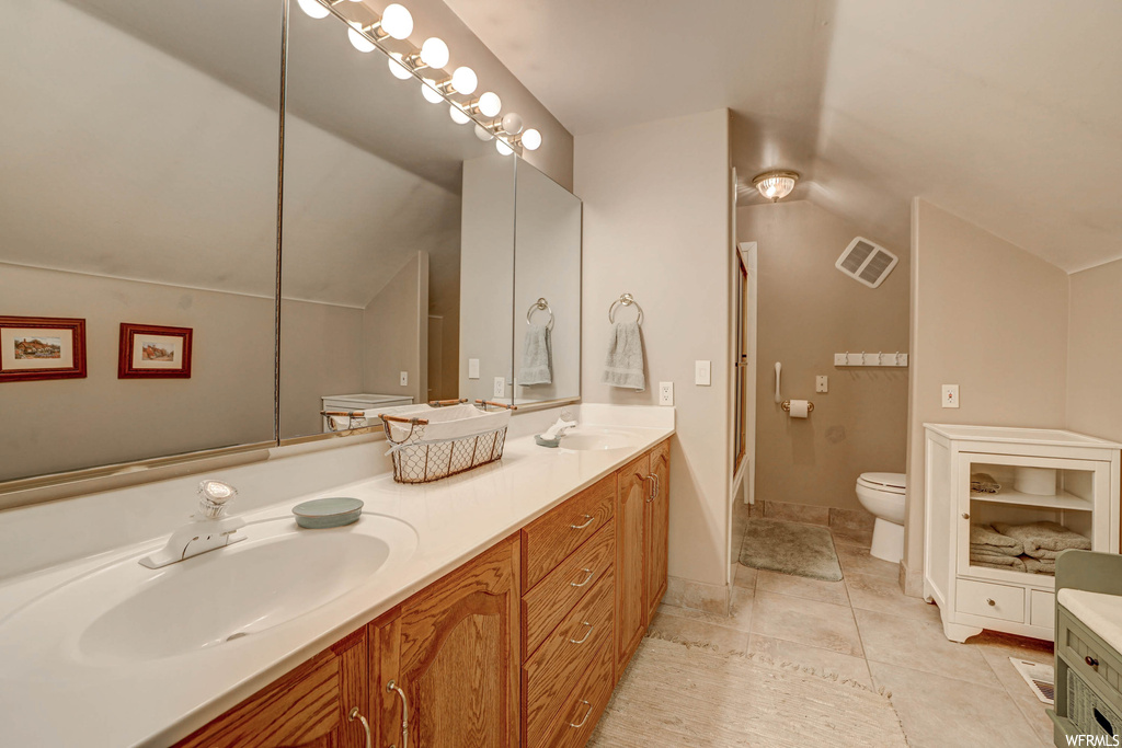 Bathroom with mirror, double vanity, light tile flooring, and lofted ceiling
