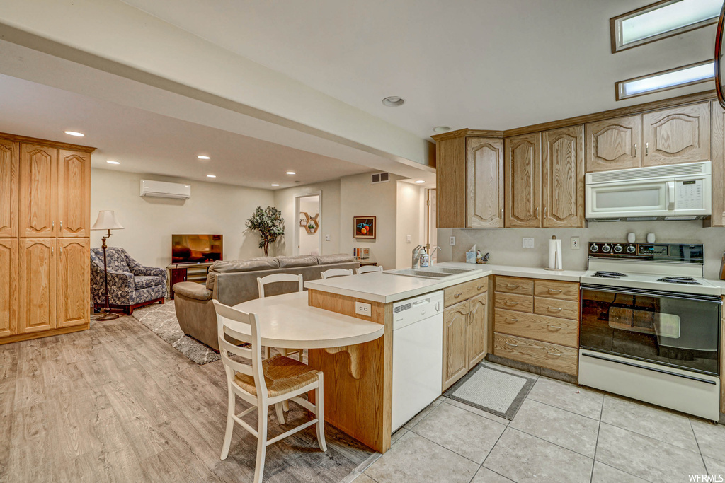 Kitchen featuring brown cabinets, light hardwood flooring, a wall unit AC, white appliances, light countertops, and backsplash