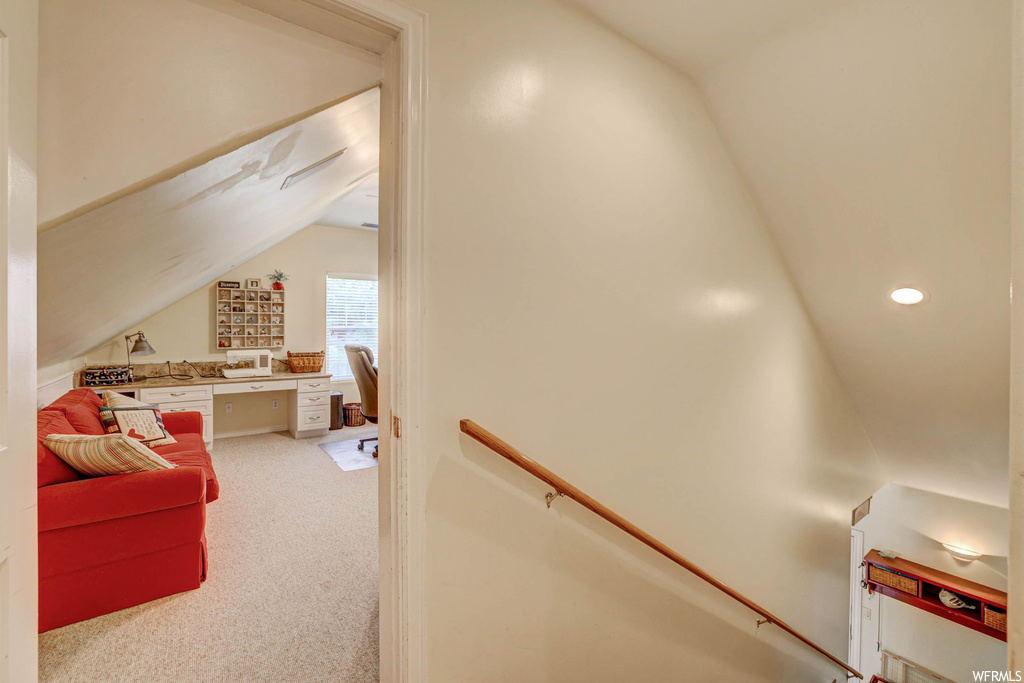 Hallway with lofted ceiling and light carpet