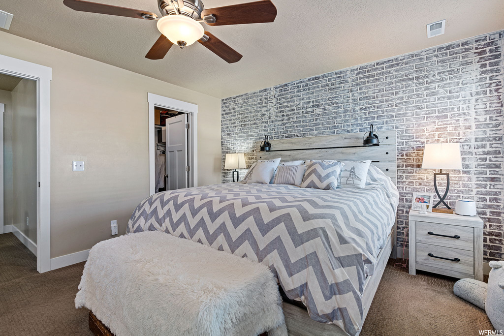 Bedroom featuring a textured ceiling, brick wall, ceiling fan, and dark carpet