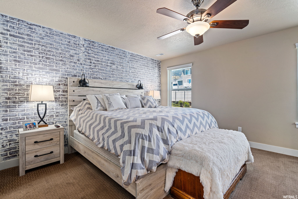 Carpeted bedroom with a textured ceiling, ceiling fan, and brick wall
