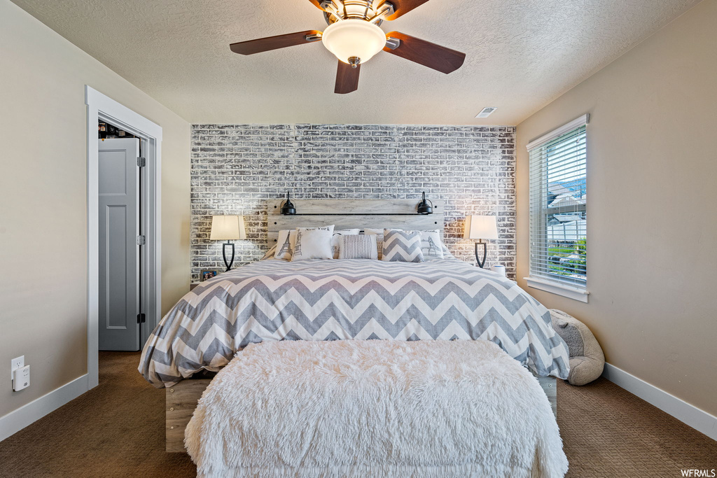 Carpeted bedroom featuring a textured ceiling, ceiling fan, and brick wall