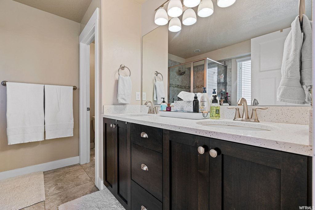 Bathroom featuring double large vanity, mirror, light tile floors, and an enclosed shower