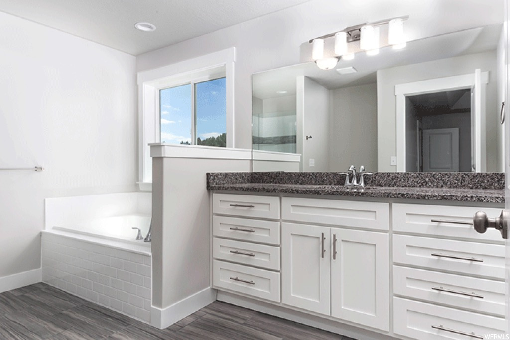 Bathroom featuring light parquet floors, vanity, tiled bath, and mirror