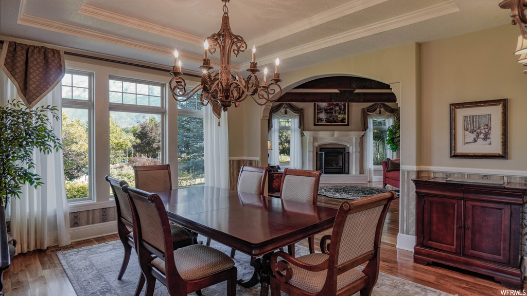 Hardwood floored dining space featuring crown molding, a notable chandelier, and a raised ceiling
