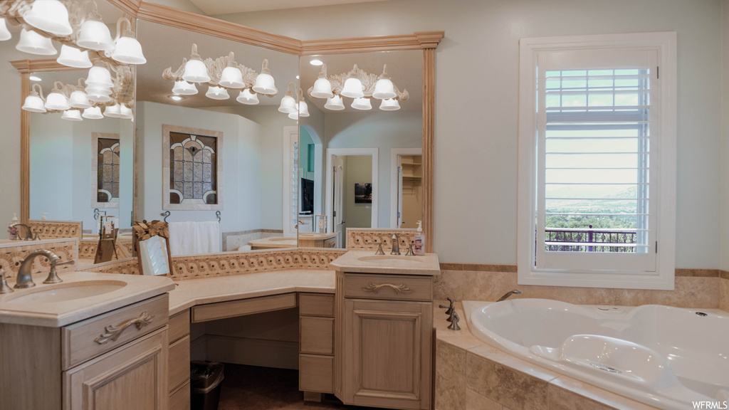 Bathroom featuring a relaxing tiled bath, crown molding, dual vanity, a wealth of natural light, and mirror