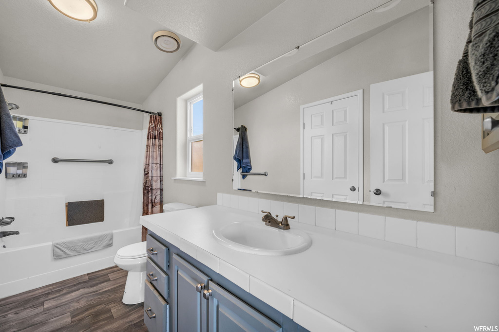 Full bathroom with oversized vanity, hardwood floors, vaulted ceiling, shower / bathtub combination with curtain, and mirror