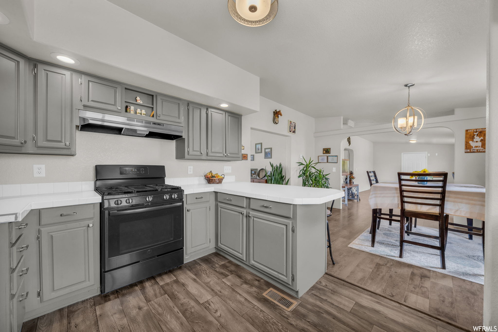 Kitchen featuring dark parquet floors, gas range oven, white cabinets, light countertops, and decorative light fixtures