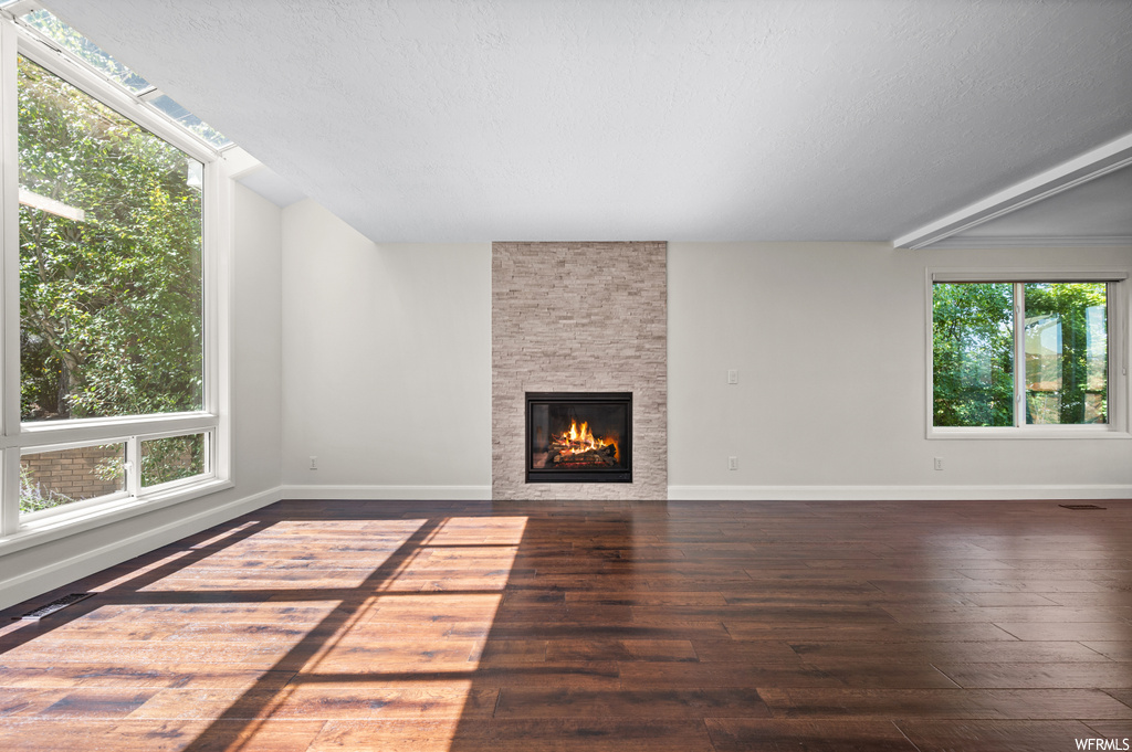 Living room with a fireplace, dark parquet floors, a textured ceiling, beam ceiling, and plenty of natural light