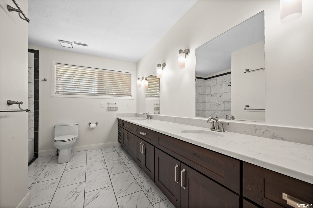 Bathroom with light tile floors, dual bowl vanity, and mirror