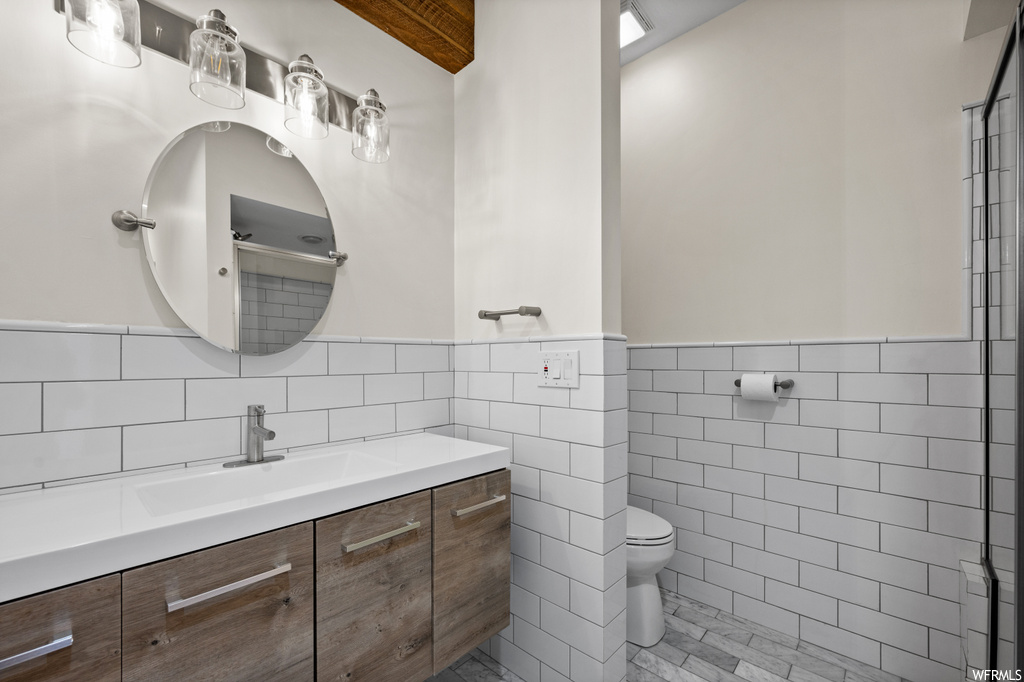 Bathroom with mirror, backsplash, light tile floors, large vanity, and tile walls