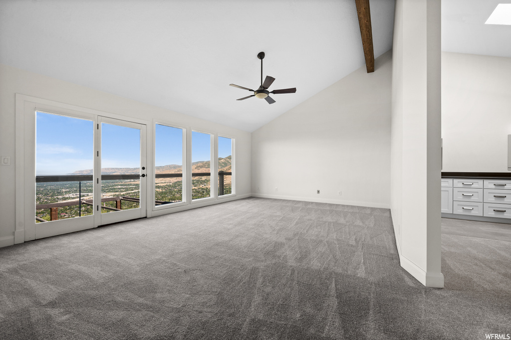 Carpeted empty room featuring lofted ceiling with beams, ceiling fan, and a high ceiling