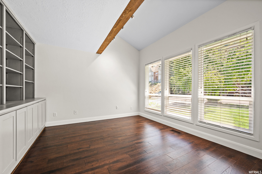 Wood floored empty room featuring vaulted ceiling with beams