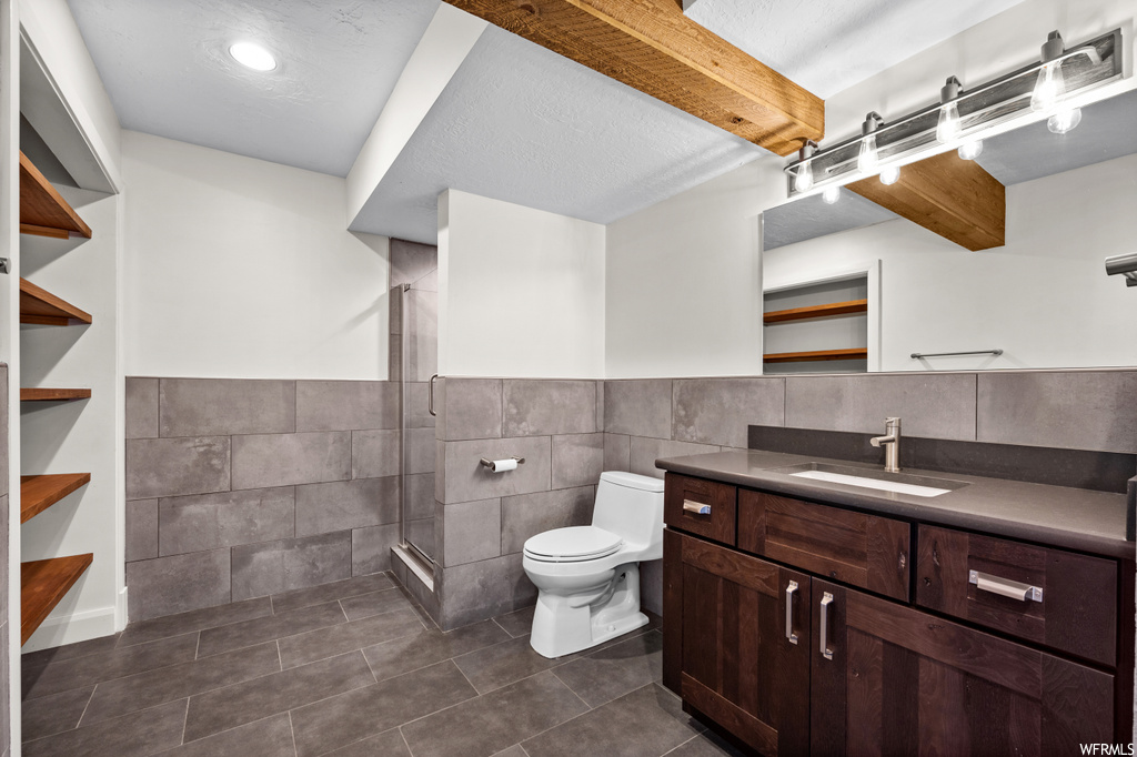 Bathroom with dark tile flooring, mirror, a textured ceiling, vanity, a shower with door, backsplash, and tile walls