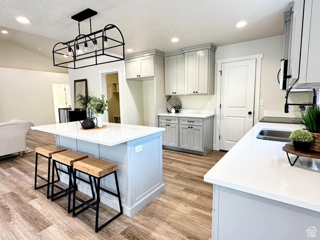 Kitchen with hanging light fixtures, sink, a center island, a kitchen bar, and light hardwood / wood-style floors