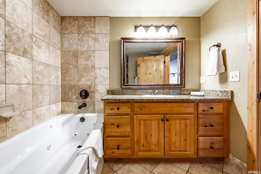 Bathroom featuring light tile floors, tile walls, mirror, vanity, and a washtub