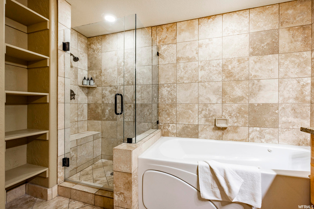 Bathroom featuring light tile floors, built in shelves, and shower with separate bathtub