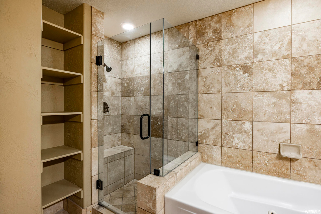Bathroom with a textured ceiling, built in shelves, and independent shower and bath