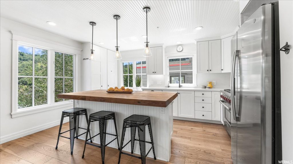 Kitchen featuring light parquet floors, a wealth of natural light, a kitchen island, white cabinets, light countertops, stainless steel fridge, and pendant lighting