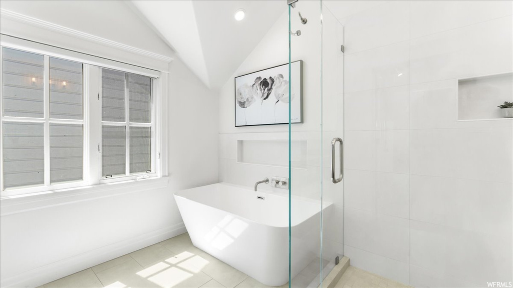 Bathroom with vaulted ceiling, light tile floors, and shower with separate bathtub