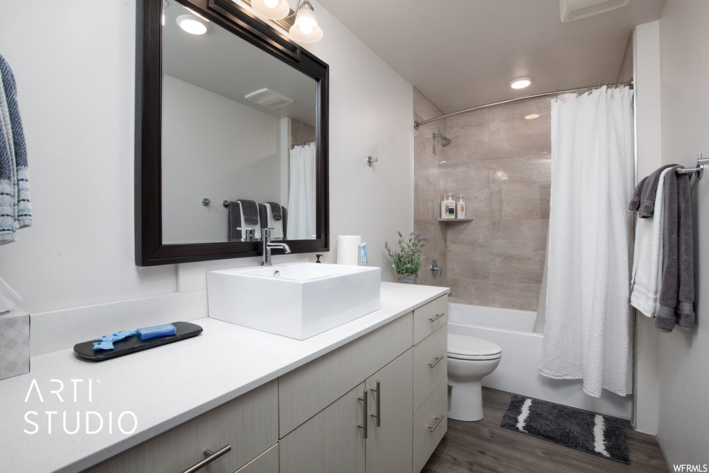 Full bathroom with dark hardwood flooring, vanity with extensive cabinet space, shower / bath combo, and mirror