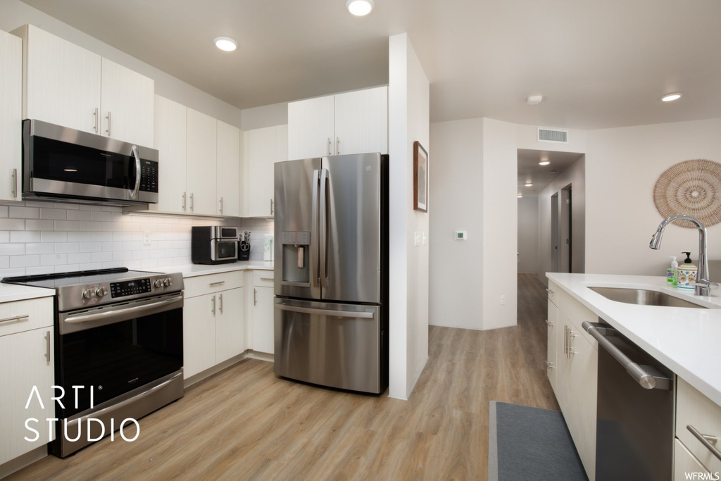 Kitchen featuring white cabinets, light countertops, backsplash, stainless steel appliances, and light hardwood floors