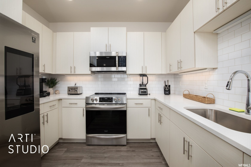 Kitchen featuring hardwood flooring, backsplash, light countertops, white cabinetry, and appliances with stainless steel finishes