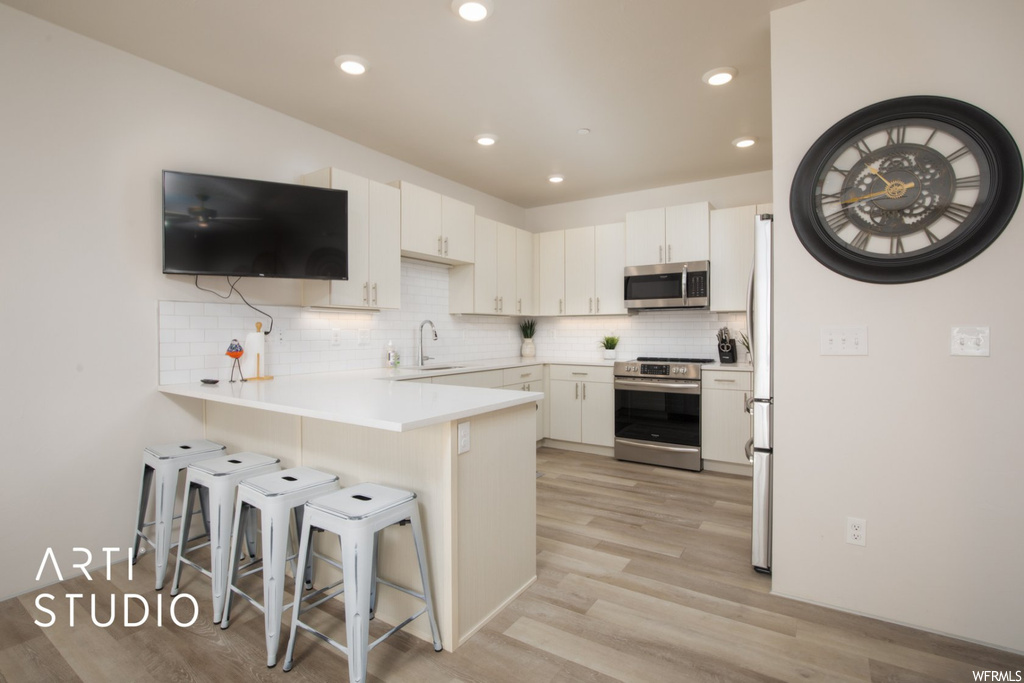 Kitchen featuring stainless steel appliances, a kitchen island, backsplash, white cabinets, light countertops, and light hardwood flooring