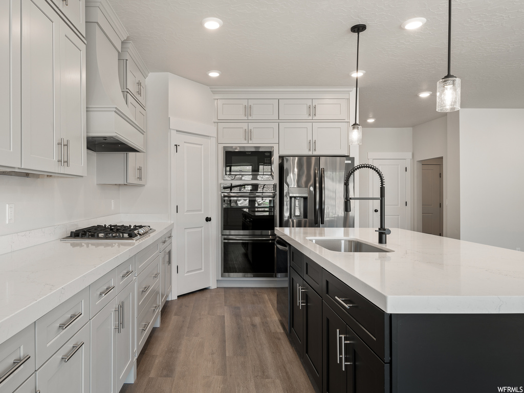 Kitchen featuring white cabinets, appliances with stainless steel finishes, dark hardwood flooring, decorative light fixtures, light countertops, and premium range hood