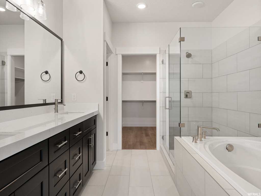 Bathroom featuring dual bowl vanity, light tile flooring, separate shower and tub, and mirror