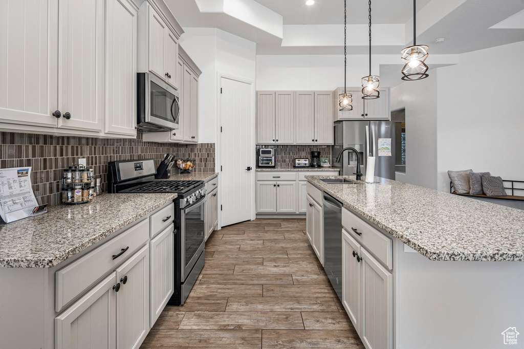 Kitchen with stainless steel appliances, a kitchen island with sink, pendant lighting, and backsplash