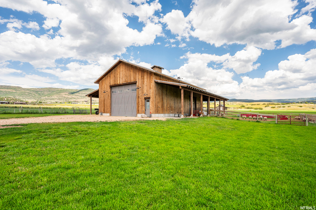Exterior space featuring a garage, a rural view, a front lawn, and a mountain view