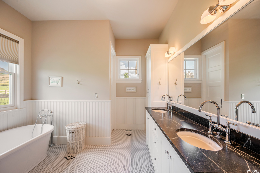 Bathroom featuring a washtub, light tile floors, mirror, and double vanity