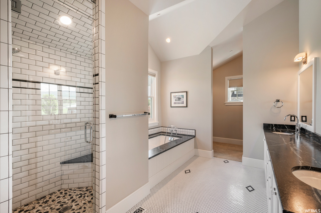 Bathroom with light tile floors, independent shower and bath, dual bowl vanity, and vaulted ceiling