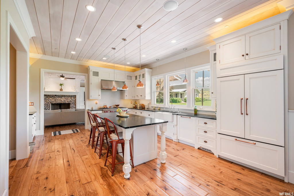 Kitchen with dark countertops, a center island, wooden ceiling, light hardwood floors, white cabinets, ornamental molding, and an island with sink