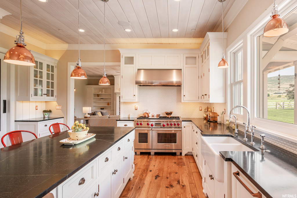 Kitchen featuring backsplash, dark countertops, hardwood floors, pendant lighting, ornamental molding, white cabinetry, and range with two ovens