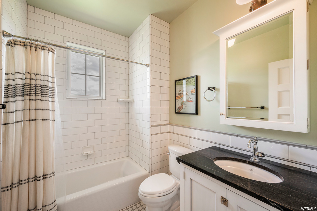 Full bathroom featuring tile walls, shower / bath combo with shower curtain, vanity, and mirror