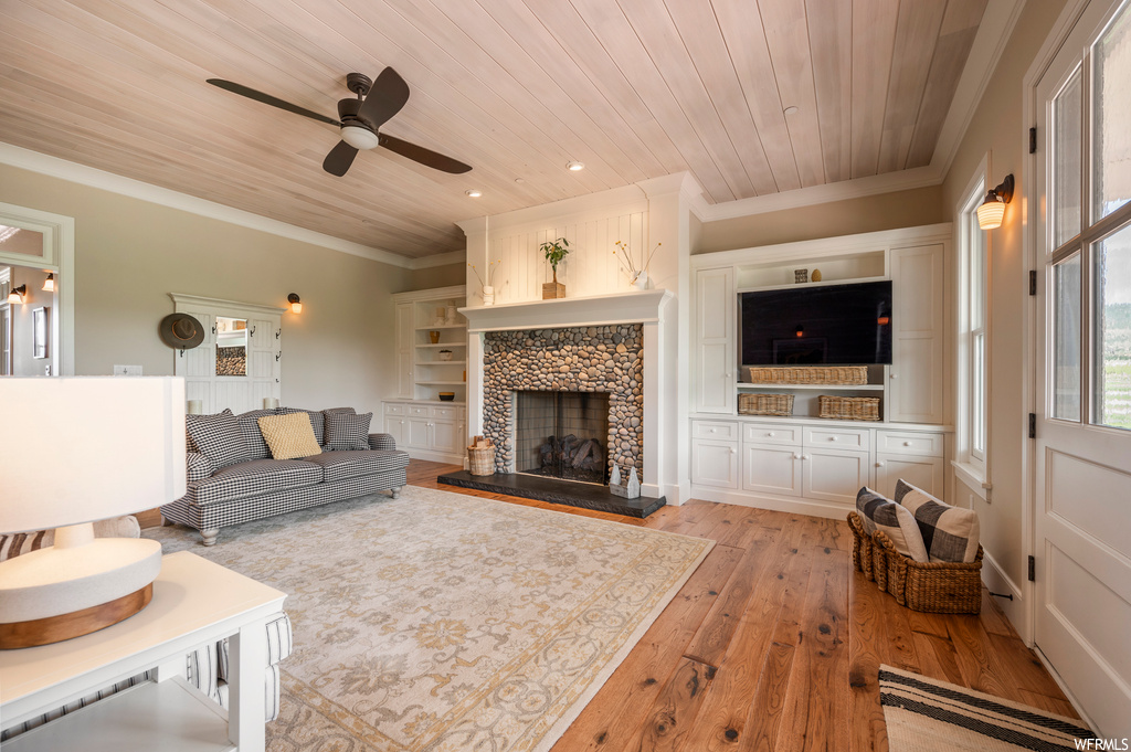 Living room featuring ceiling fan, built in shelves, light hardwood floors, wood ceiling, ornamental molding, and a fireplace