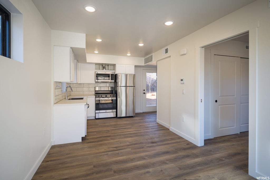 Kitchen with sink, appliances with stainless steel finishes, white cabinets, dark hardwood / wood-style flooring, and backsplash