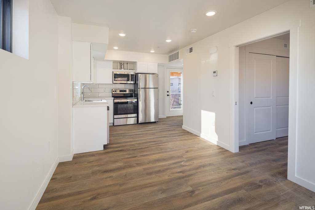 Kitchen with sink, appliances with stainless steel finishes, dark wood-type flooring, white cabinets, and backsplash