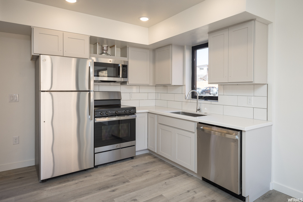 Kitchen featuring backsplash, sink, stainless steel appliances, and light hardwood / wood-style floors