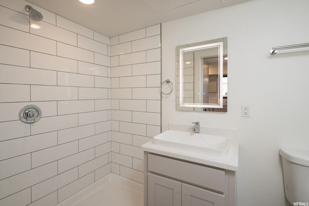 Bathroom featuring toilet, vanity with extensive cabinet space, and tiled shower