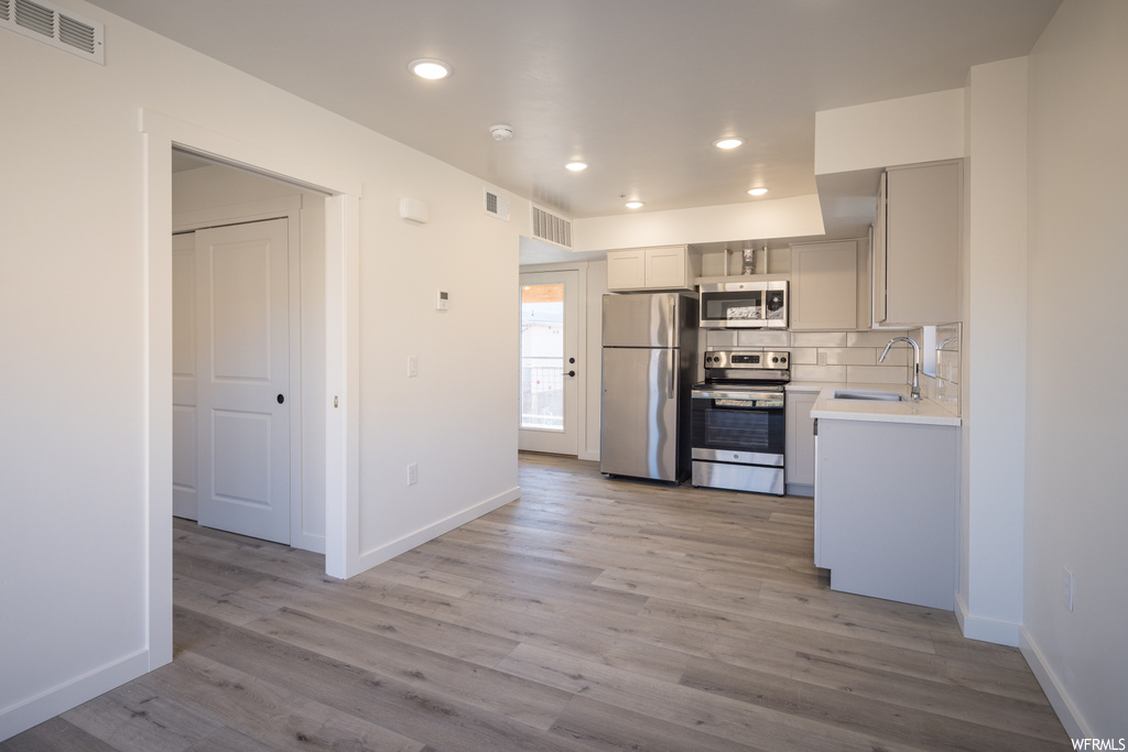 Kitchen featuring sink, light hardwood / wood-style floors, stainless steel appliances, and backsplash