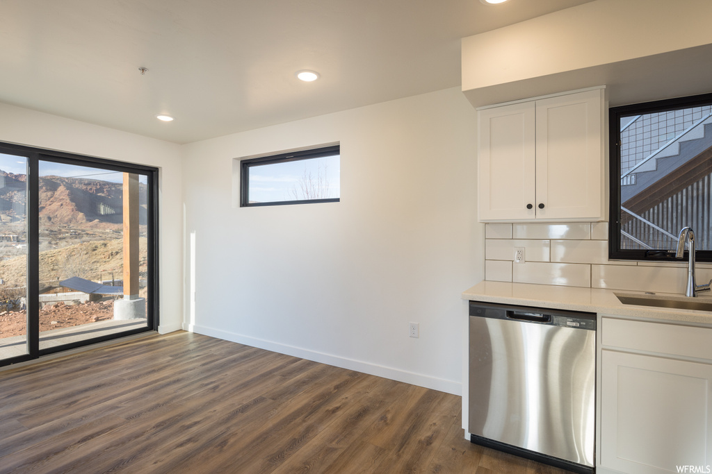 Kitchen with dark hardwood / wood-style floors, stainless steel dishwasher, tasteful backsplash, and white cabinetry