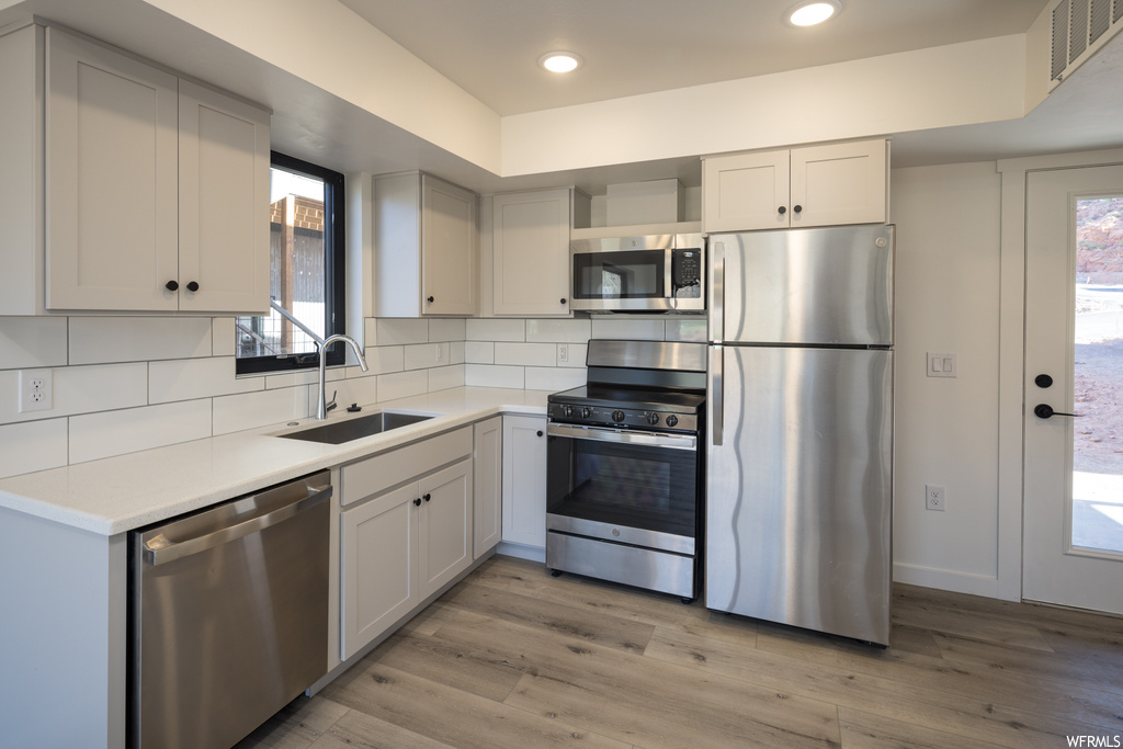 Kitchen featuring stainless steel appliances, backsplash, white cabinets, light countertops, and light parquet floors