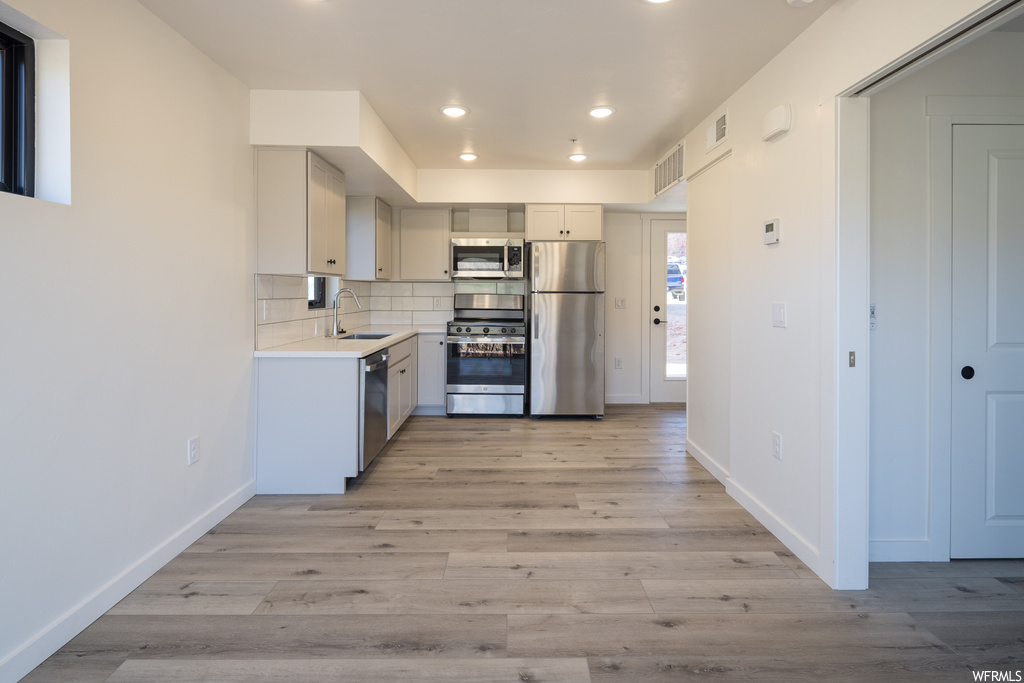 Kitchen featuring backsplash, light hardwood floors, appliances with stainless steel finishes, light countertops, and white cabinetry